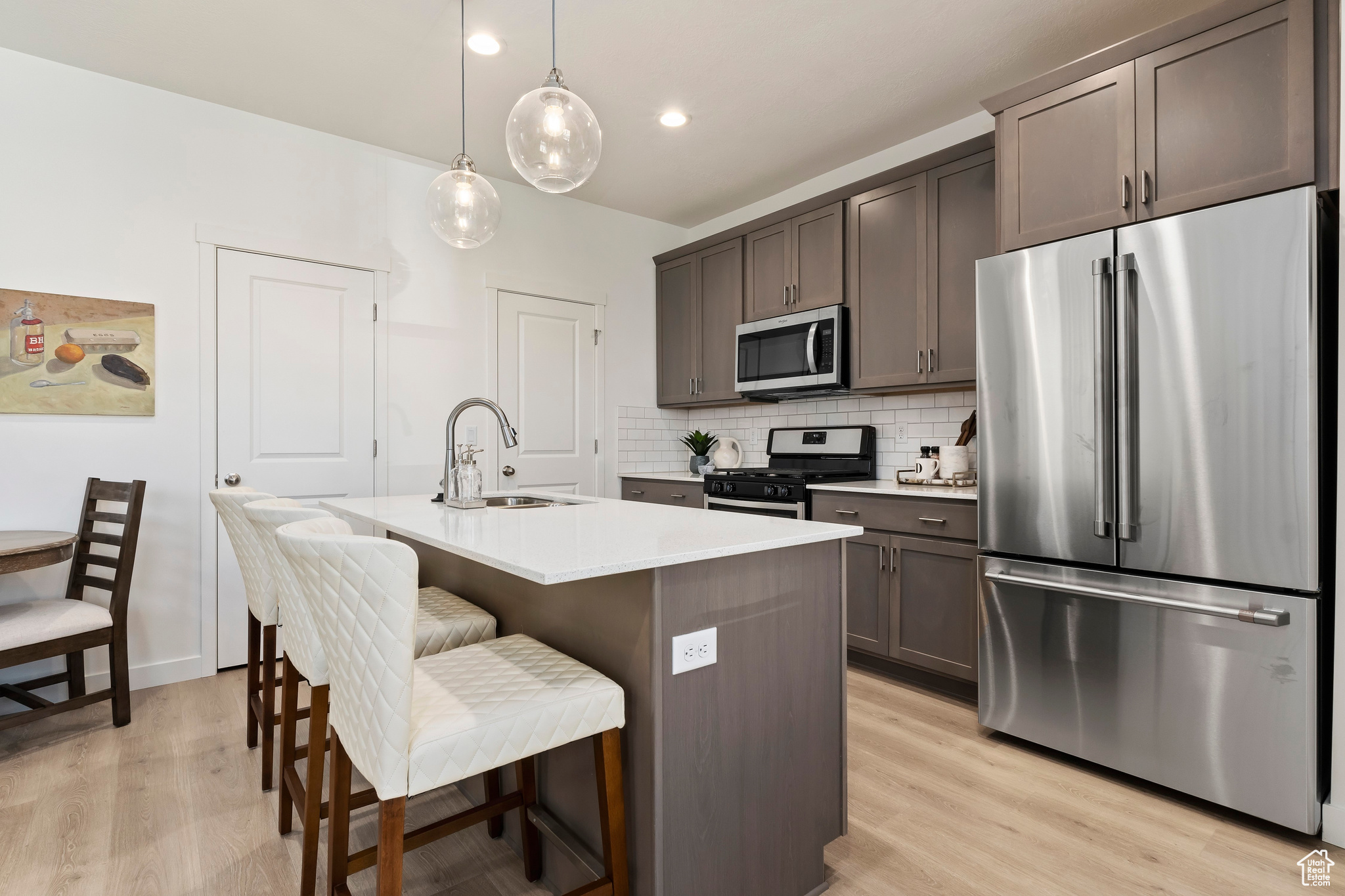 Kitchen featuring appliances with stainless steel finishes, light hardwood / wood-style flooring, hanging light fixtures, tasteful backsplash, and sink