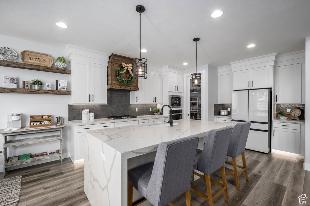 Kitchen with stainless steel appliances, tasteful backsplash, dark wood-type flooring, a waterfall quartz kitchen island with sink, and pendant lighting