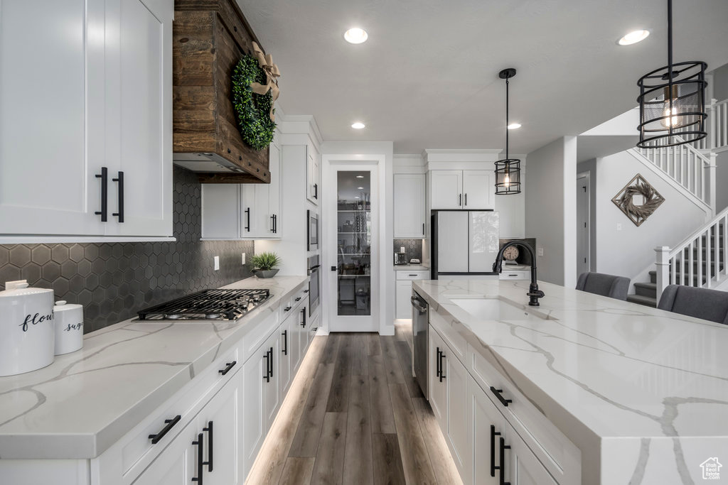 Kitchen with appliances with stainless steel finishes, tasteful backsplash, custom range hood, hardwood / wood-style flooring, and pendant lighting