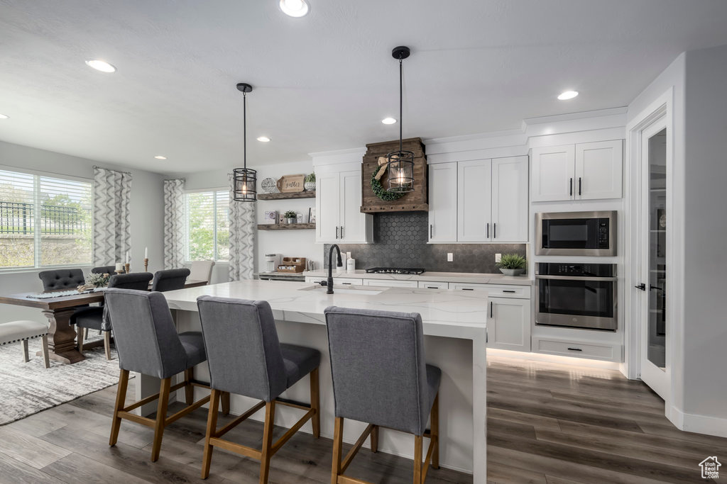 Kitchen featuring white cabinets, dark hardwood / wood-style flooring, decorative light fixtures, quartz countertops/island and stainless steel appliances
