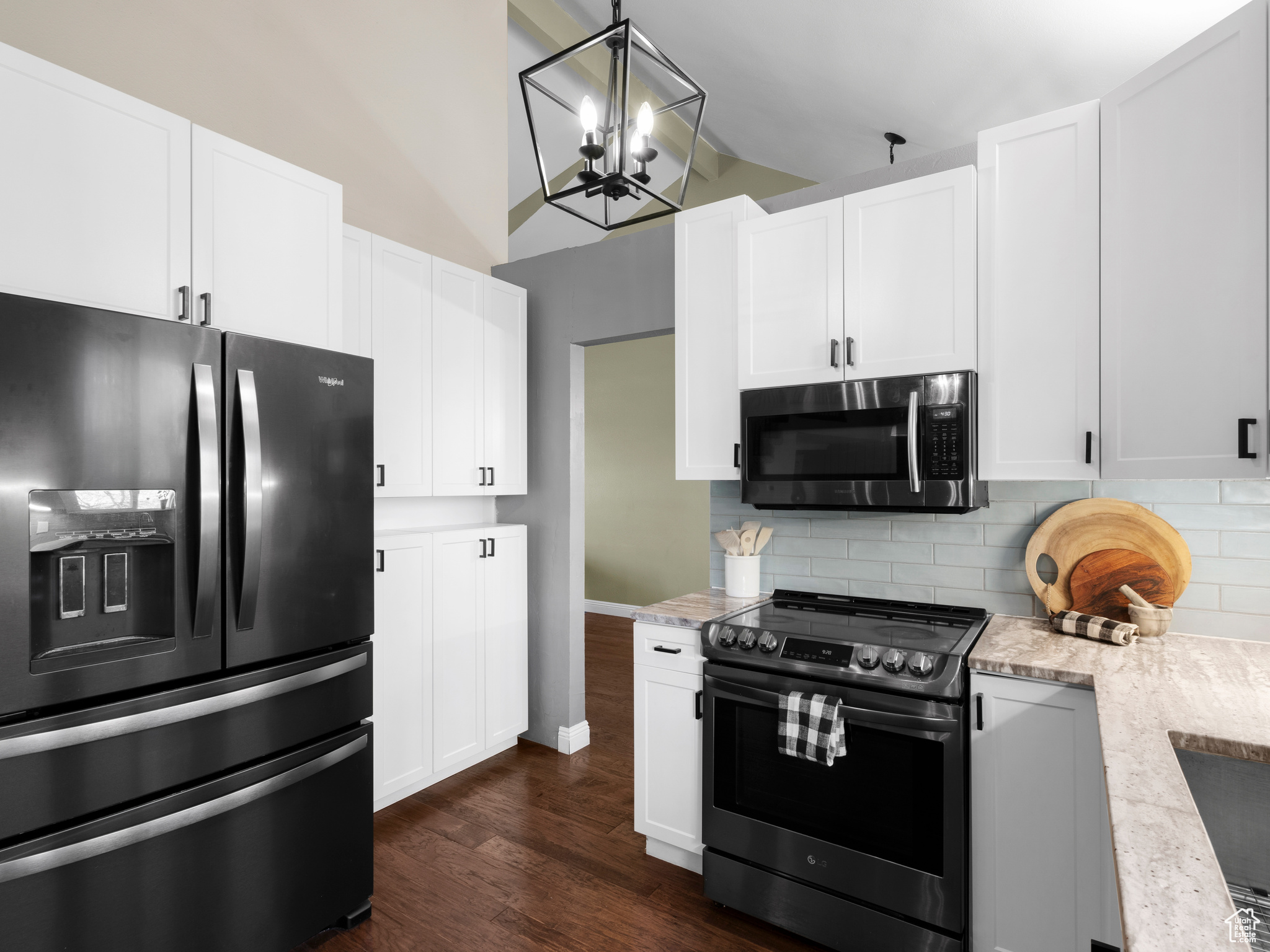 Kitchen with black refrigerator with ice dispenser, tasteful backsplash, dark wood-type flooring, white cabinets, and range with electric cooktop