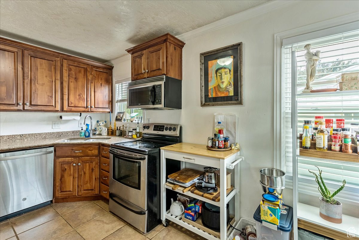 Kitchen featuring sink, stainless steel appliances, light tile floors, and ornamental molding