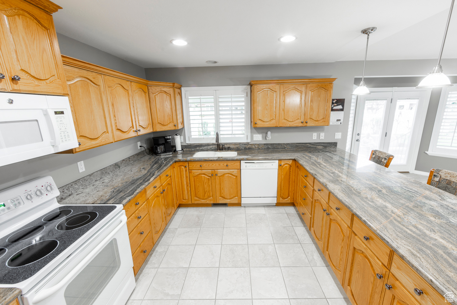 Kitchen with white appliances, pendant lighting, sink, granite counters, and light tile floors