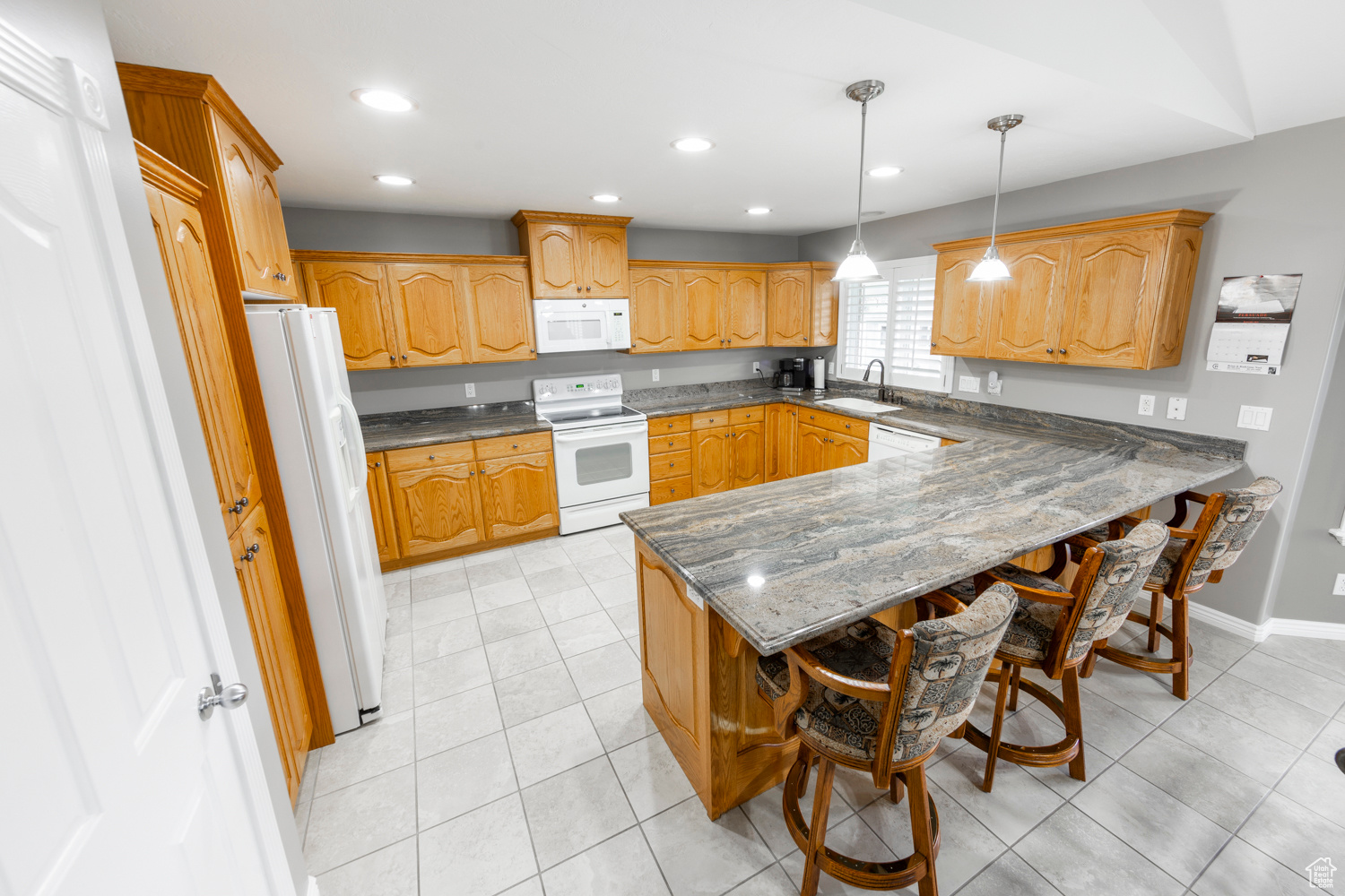 Kitchen featuring pendant lighting, white appliances, light tile flooring, a kitchen bar, gorgeous granite counters, and  a double sink
