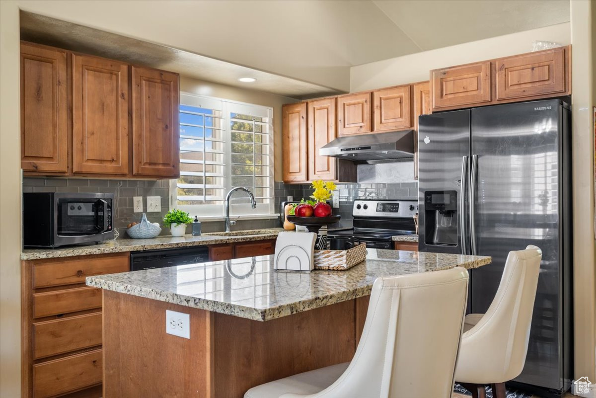 Kitchen with appliances with stainless steel finishes, backsplash, a center island, and a kitchen breakfast bar