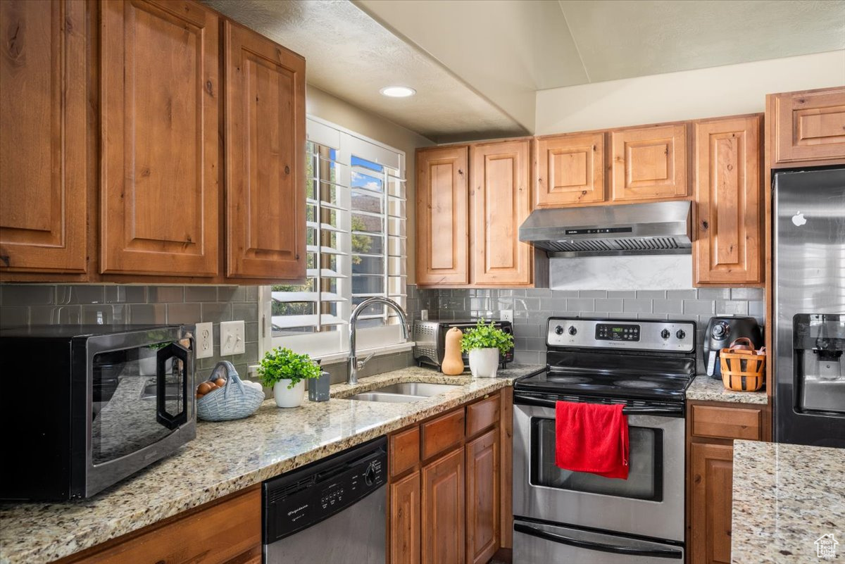 Kitchen with sink, appliances with stainless steel finishes, tasteful backsplash, and light stone counters
