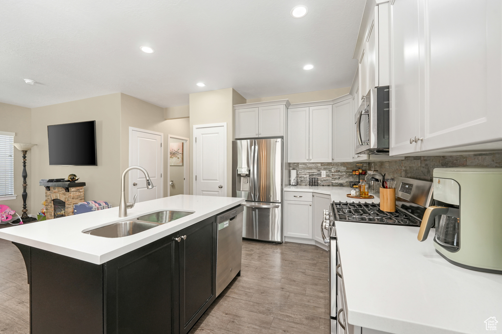 Kitchen featuring appliances with stainless steel finishes, a center island with sink, tasteful backsplash, sink, and light wood-type flooring
