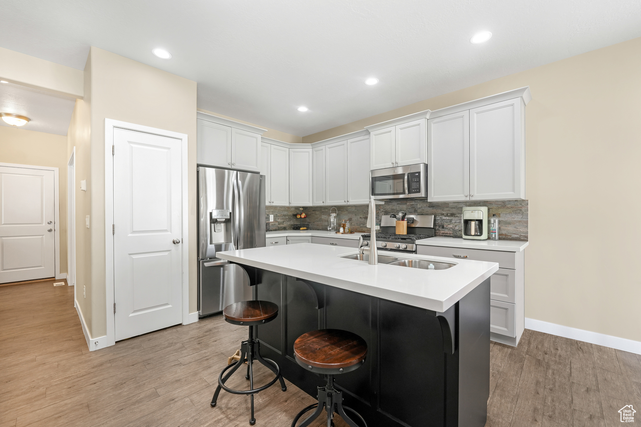 Kitchen featuring appliances with stainless steel finishes, backsplash, light wood-type flooring, and white cabinetry