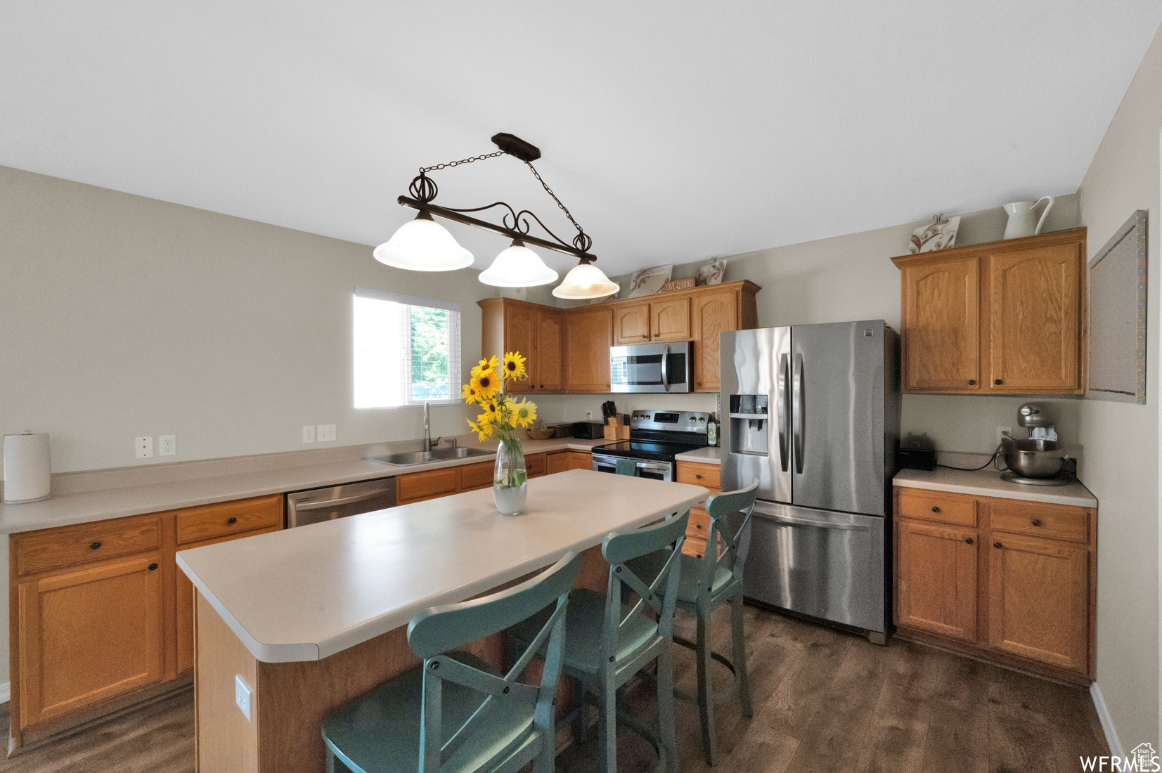 Kitchen with a center island, dark wood-type flooring, stainless steel appliances, and decorative light fixtures
