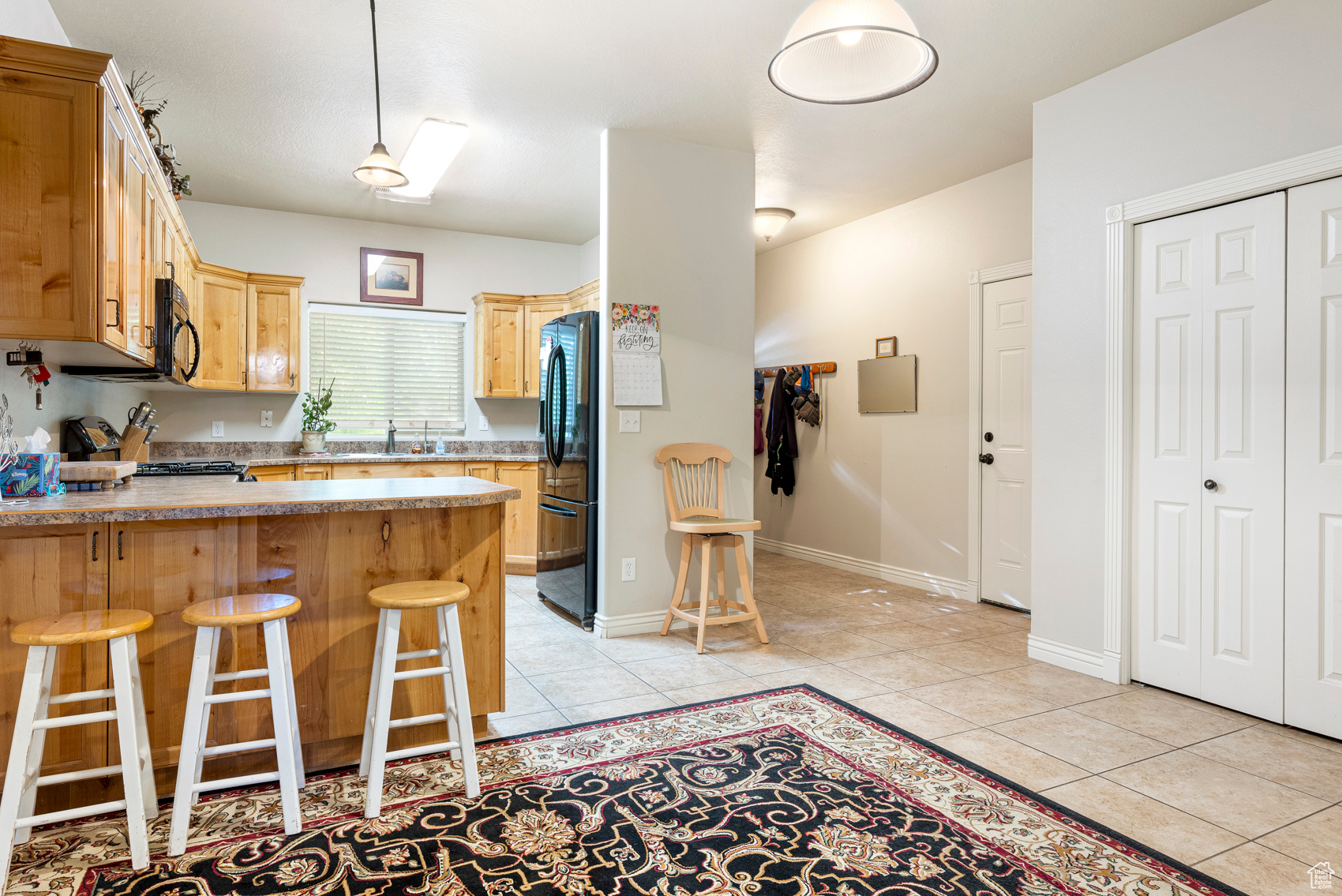 Kitchen with kitchen peninsula, a kitchen bar, black appliances, sink, and light tile floors