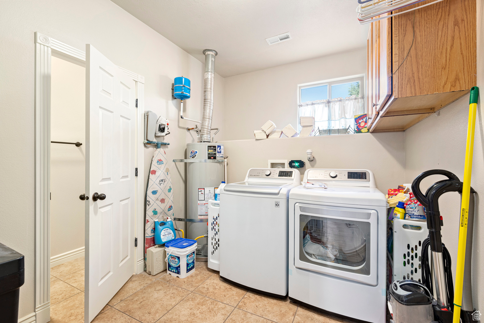 Clothes washing area featuring light tile flooring, cabinets, strapped water heater, and washer and dryer