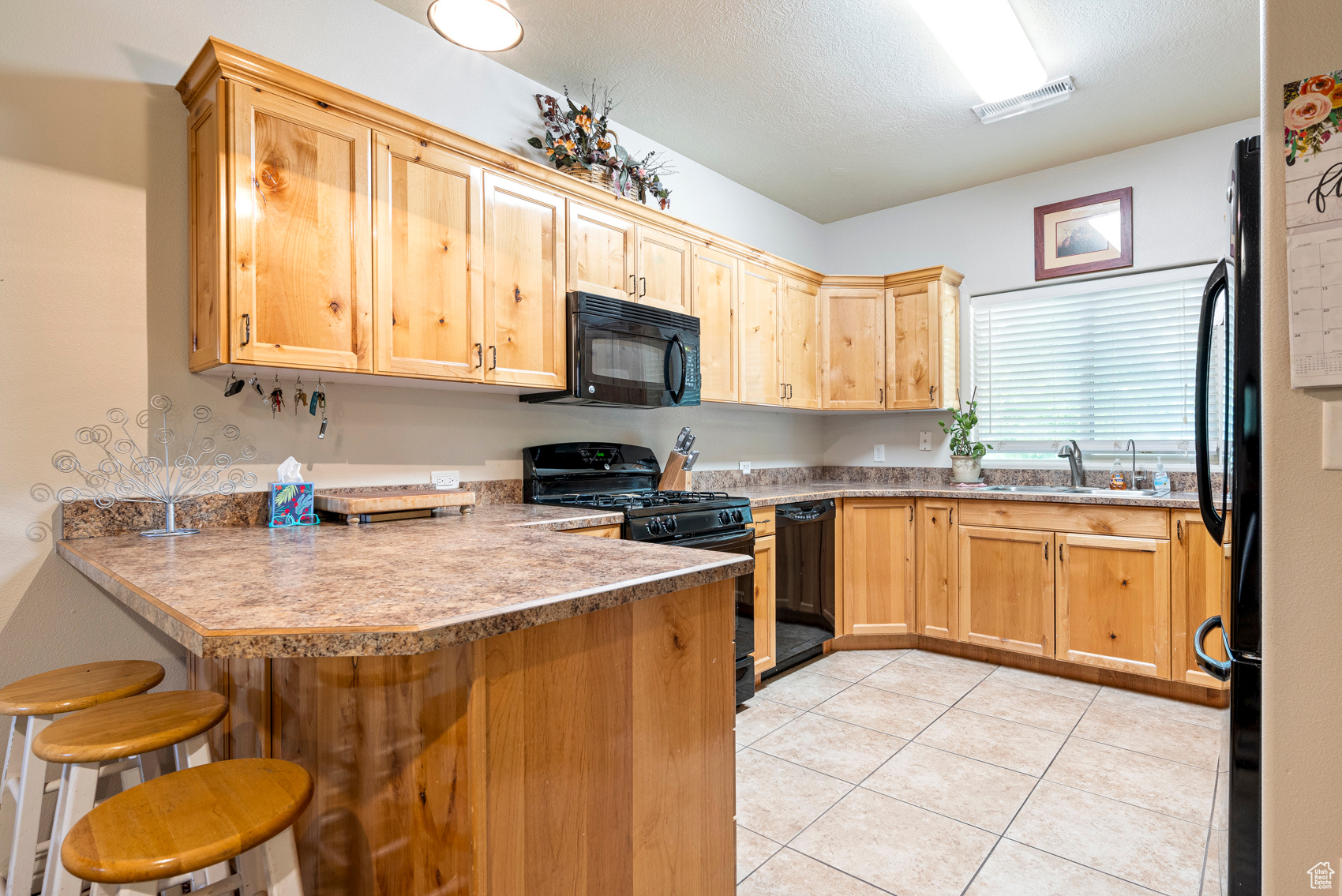 Kitchen with kitchen peninsula, a breakfast bar area, light tile flooring, black appliances, and sink