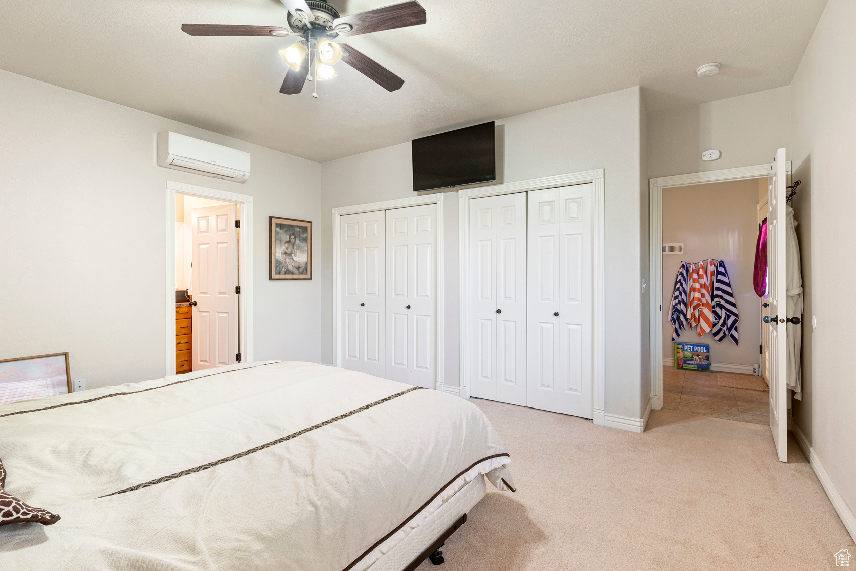 Carpeted bedroom with a wall mounted AC, ceiling fan, and two closets