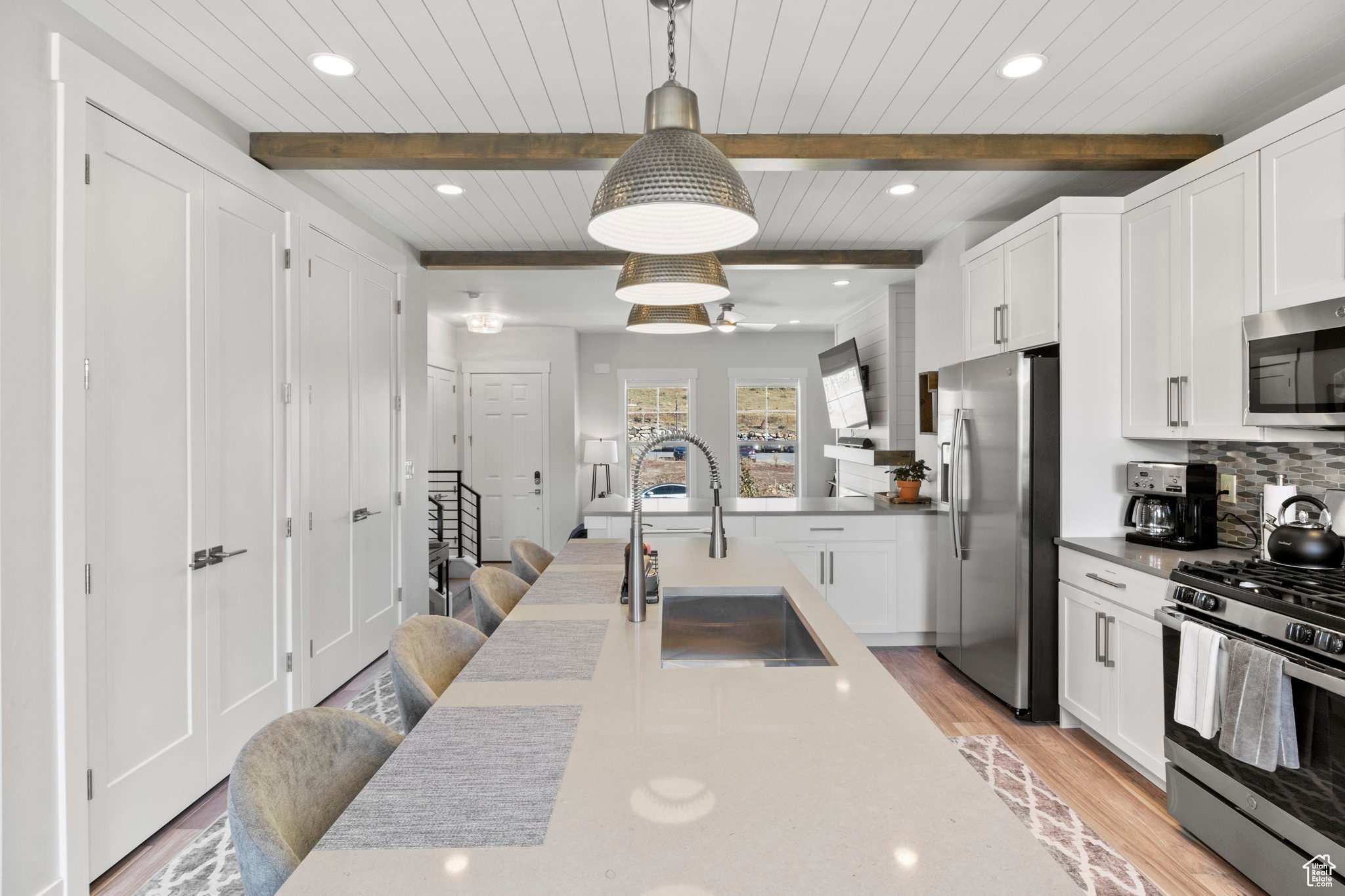 Kitchen with beamed ceiling, appliances with stainless steel finishes, light hardwood / wood-style floors, tasteful backsplash, and pendant lighting