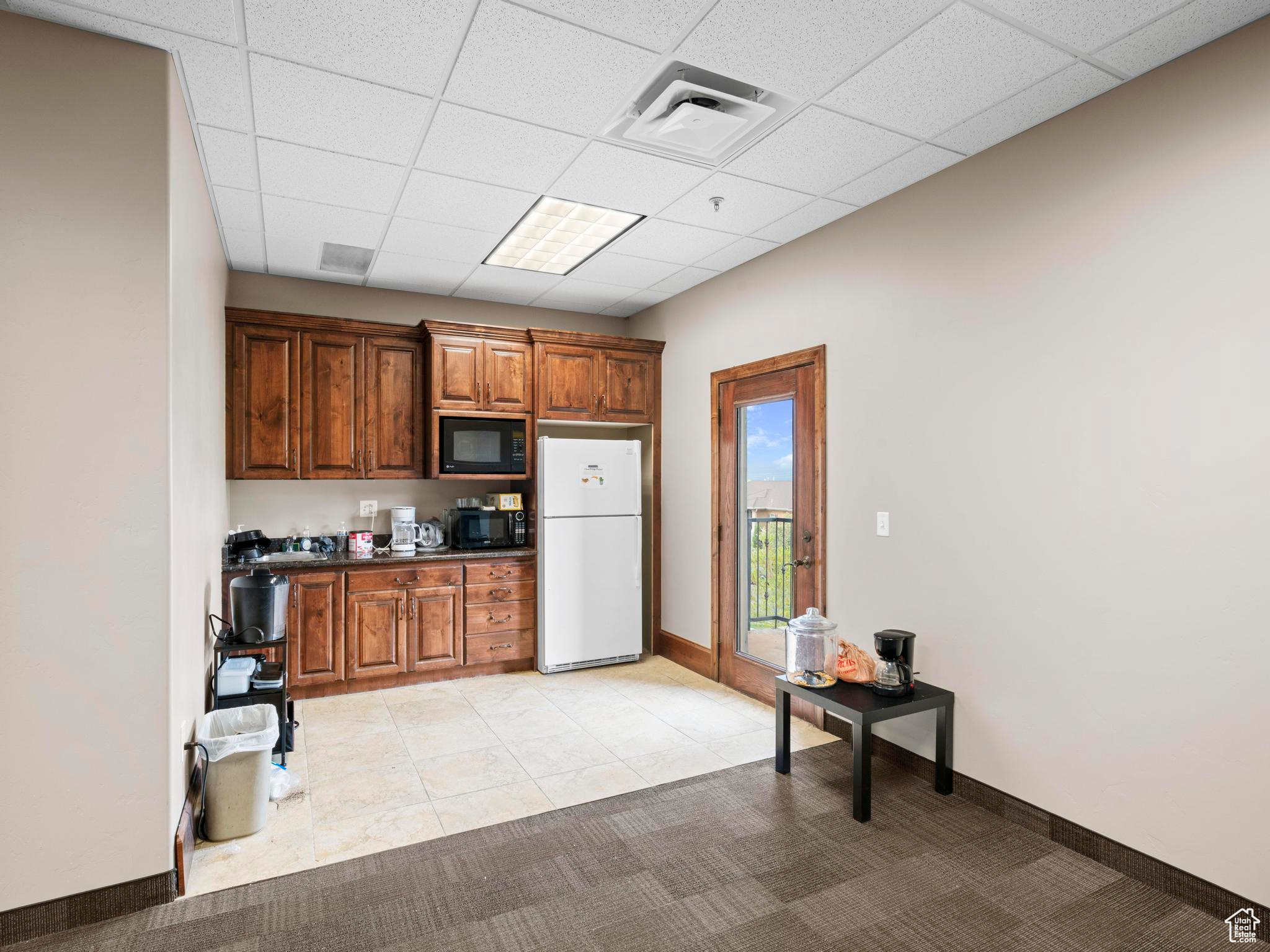 Kitchen featuring a drop ceiling, white refrigerator, black microwave, and light carpet