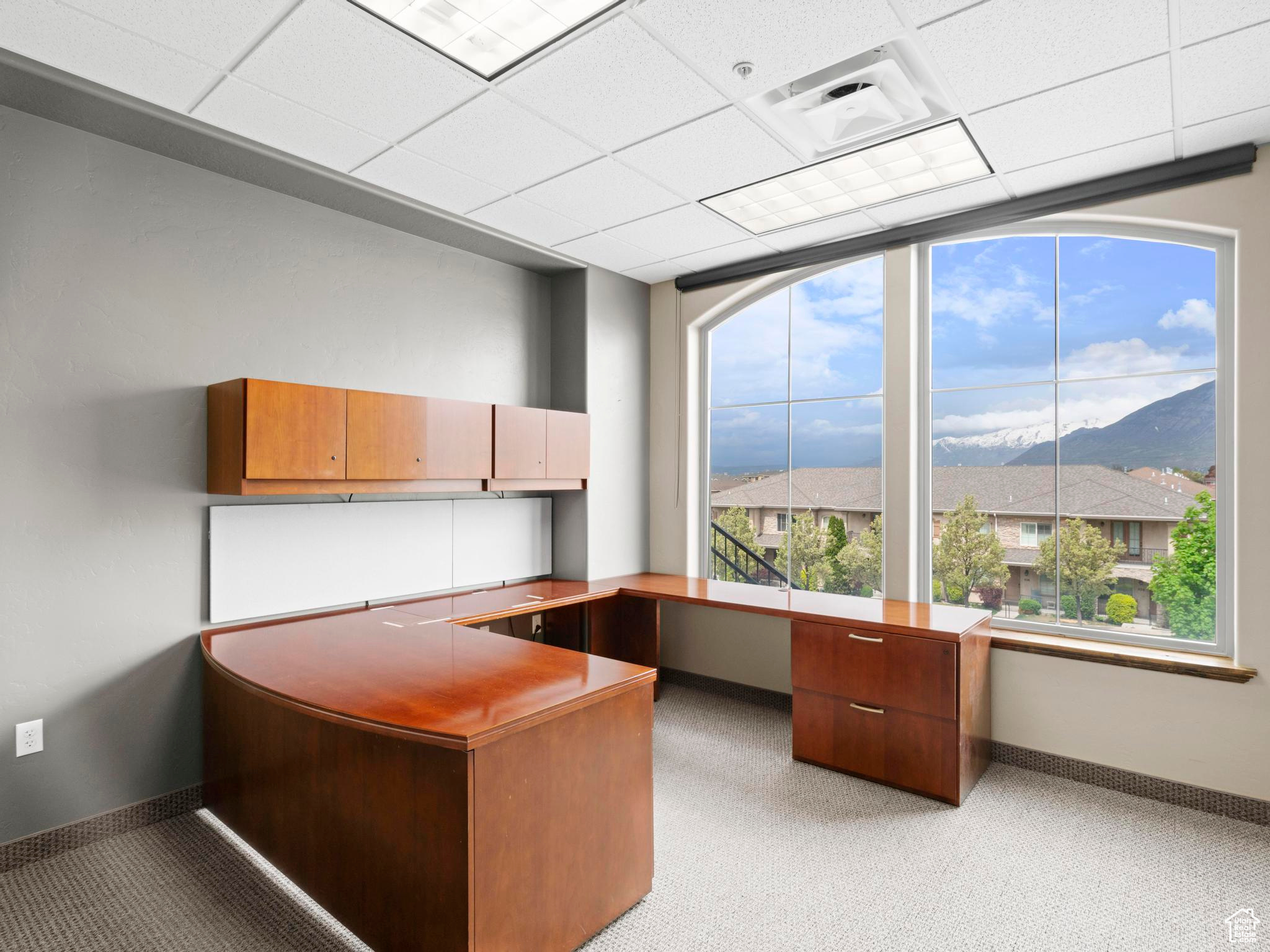 Carpeted office space featuring a drop ceiling and built in desk