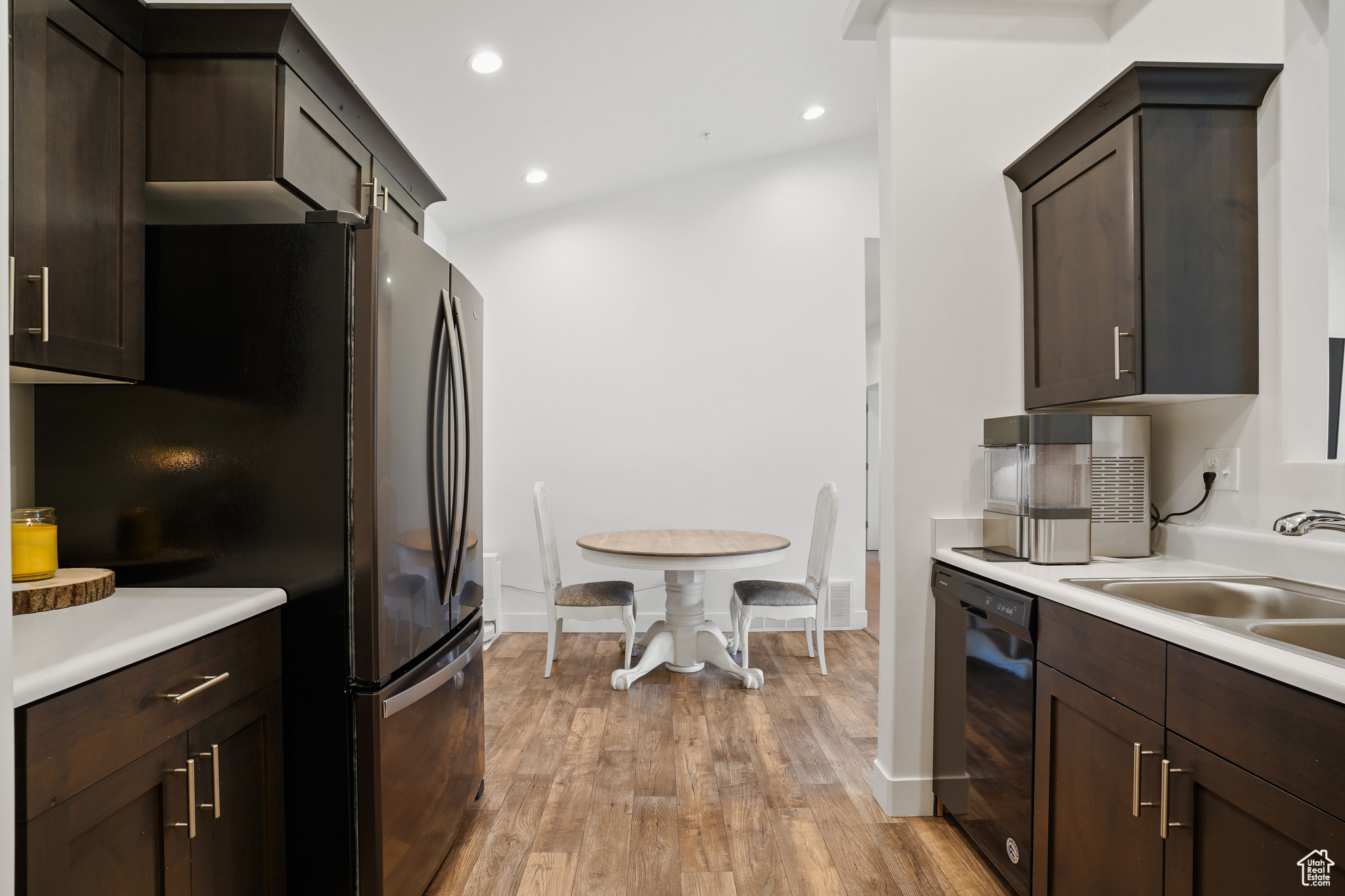 Kitchen featuring dark brown cabinets, vaulted ceiling, dishwasher, sink, and light wood-type flooring