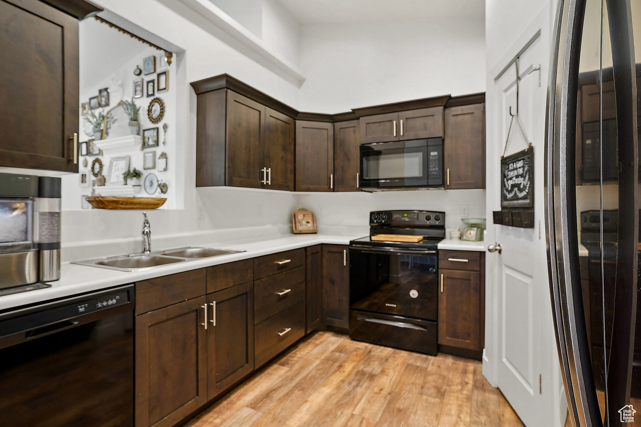 Kitchen with light hardwood / wood-style flooring, sink, dark brown cabinetry, and black appliances