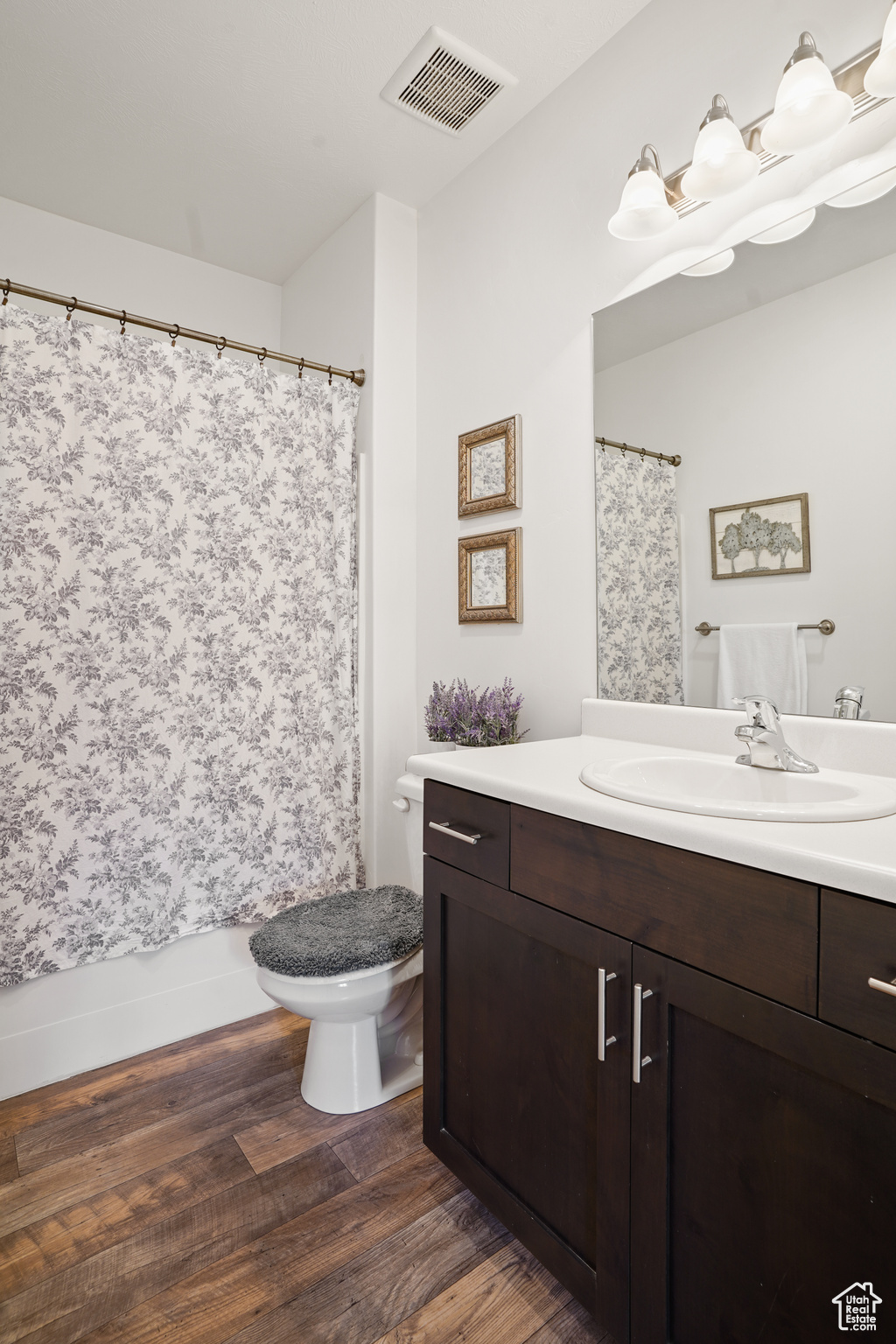 Full bathroom with hardwood / wood-style floors, vanity, shower / bath combo, and toilet