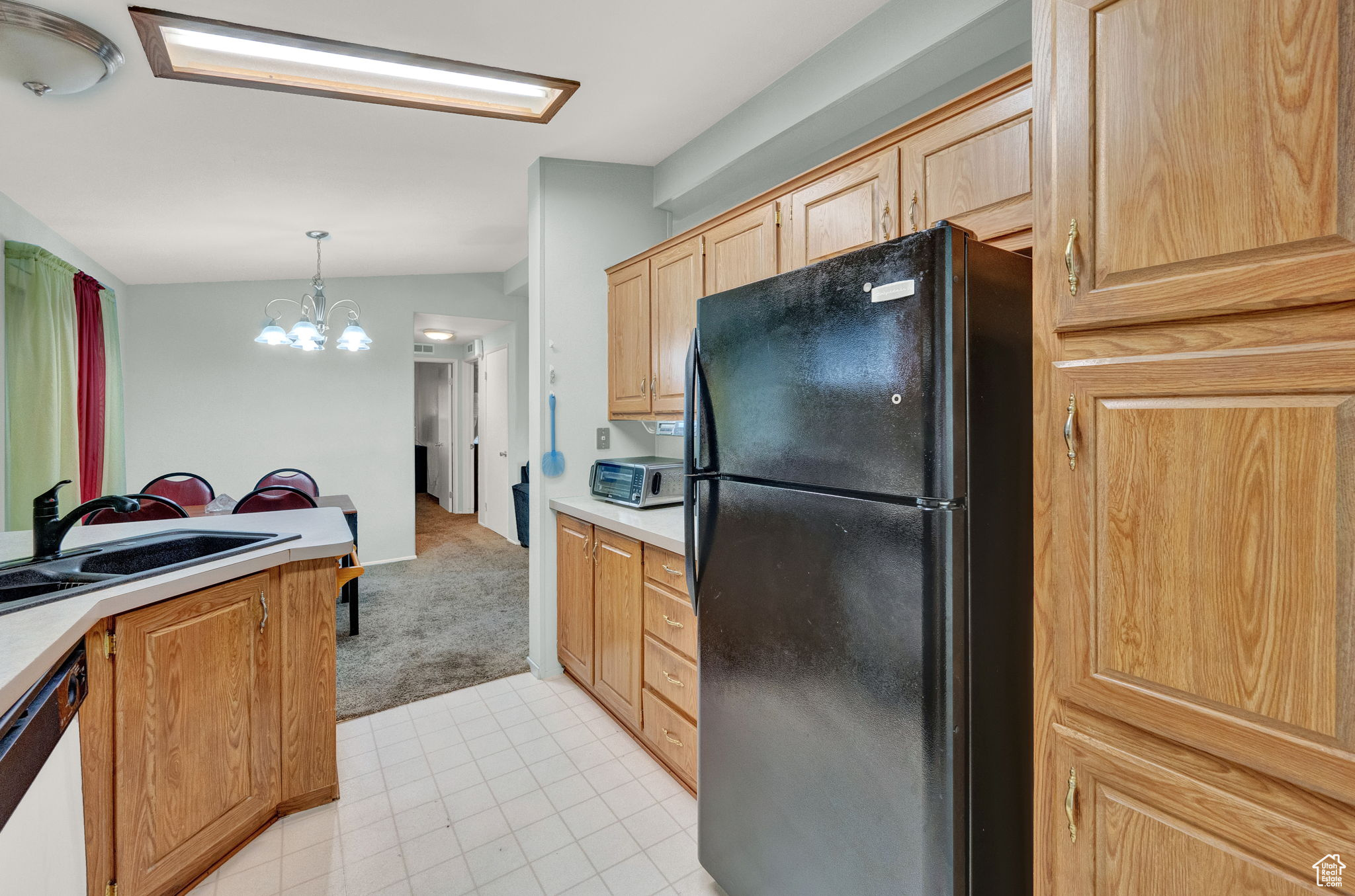 Kitchen featuring a notable chandelier, dishwasher, light tile flooring, black fridge, and decorative light fixtures