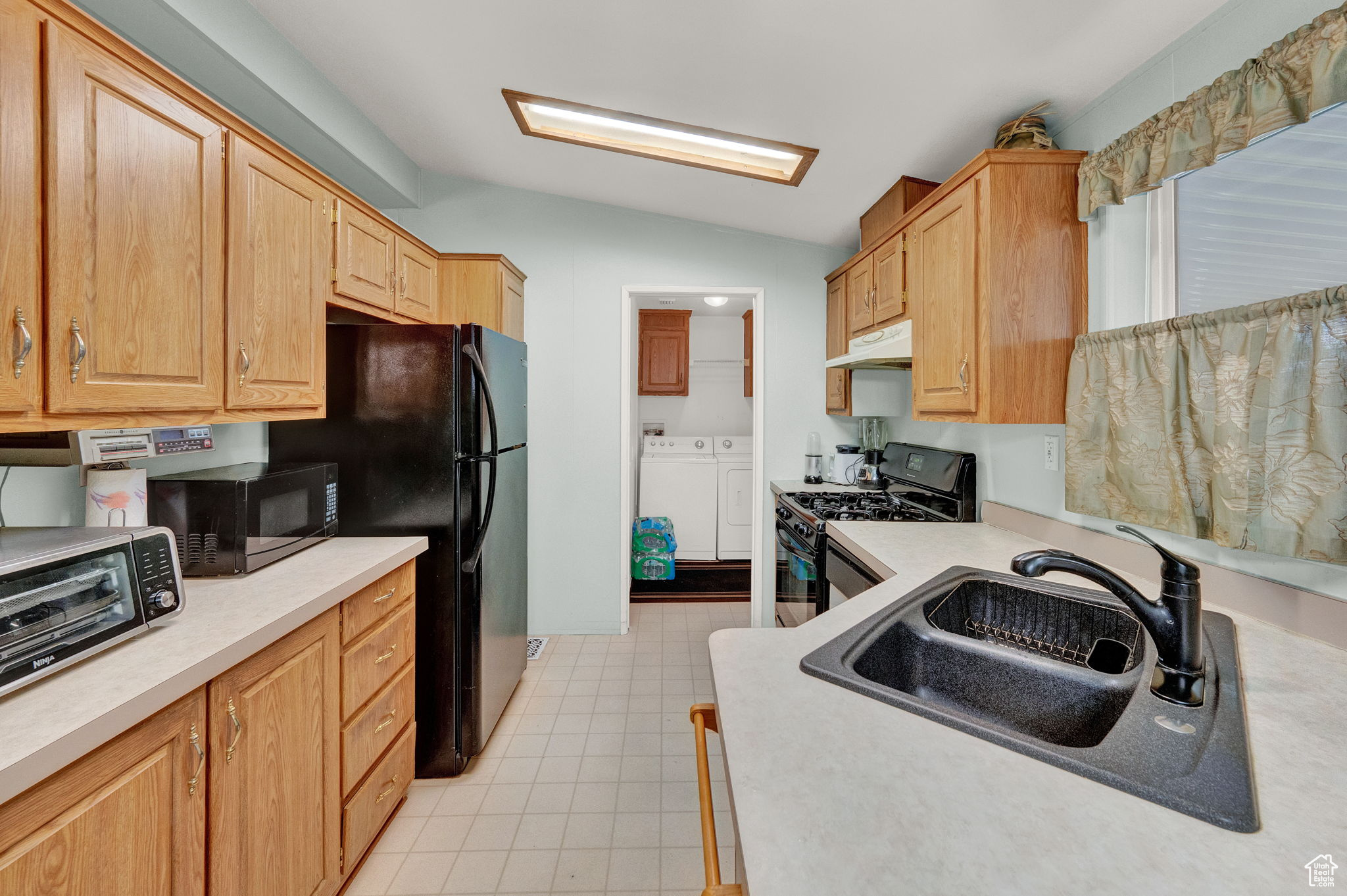 Kitchen with gas range oven, washing machine and clothes dryer, sink, light tile floors, and lofted ceiling