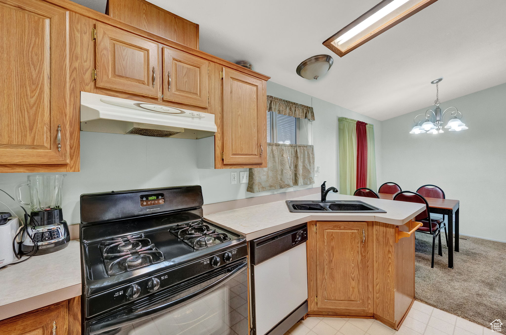 Kitchen with black gas range oven, sink, dishwasher, light colored carpet, and an inviting chandelier