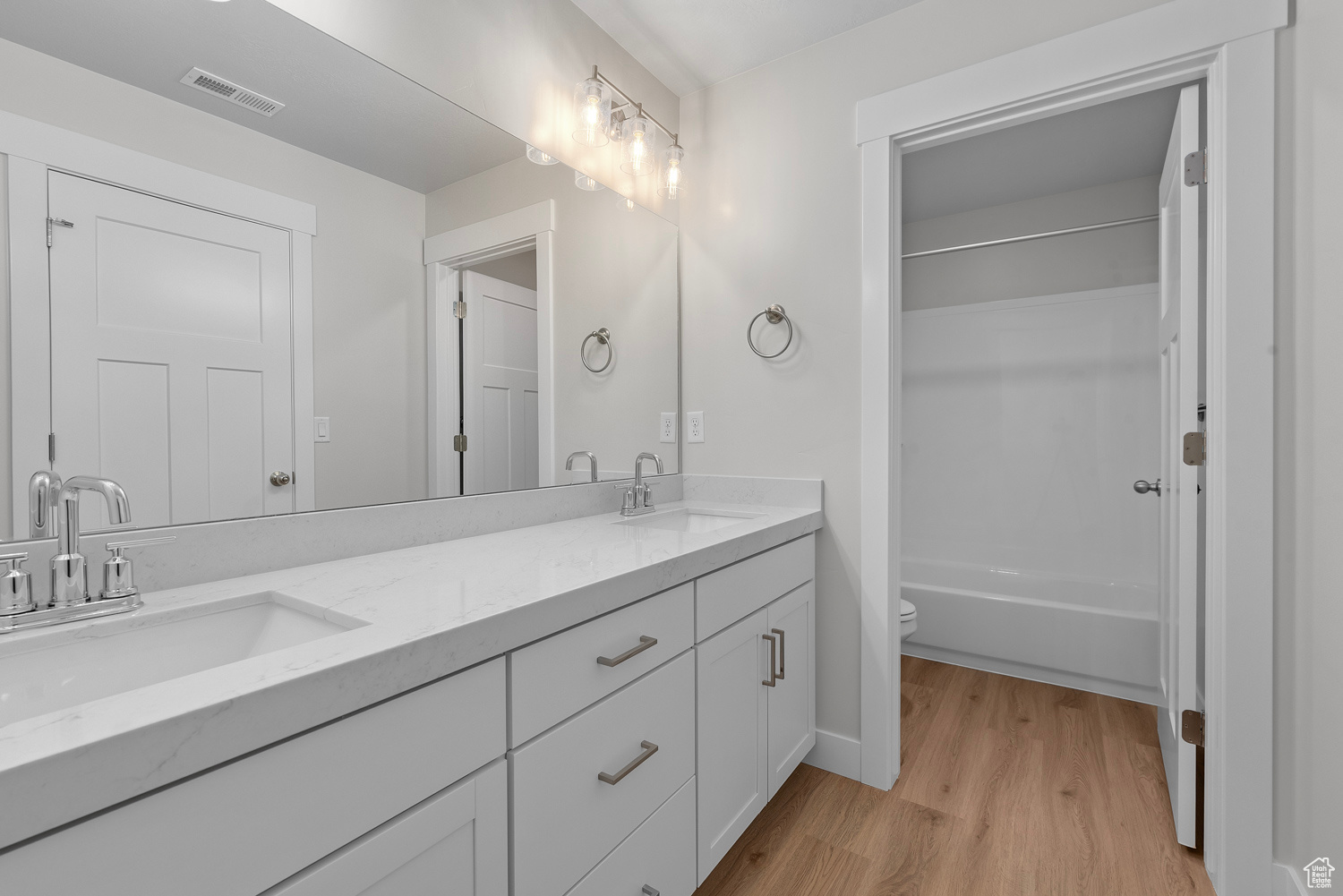 Full bathroom featuring vanity with extensive cabinet space, wood-type flooring, shower / tub combination, dual sinks, and toilet