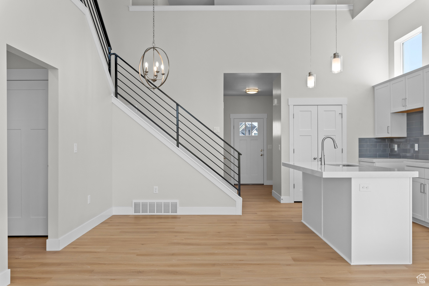 Kitchen with backsplash, light hardwood / wood-style flooring, a high ceiling, and hanging light fixtures