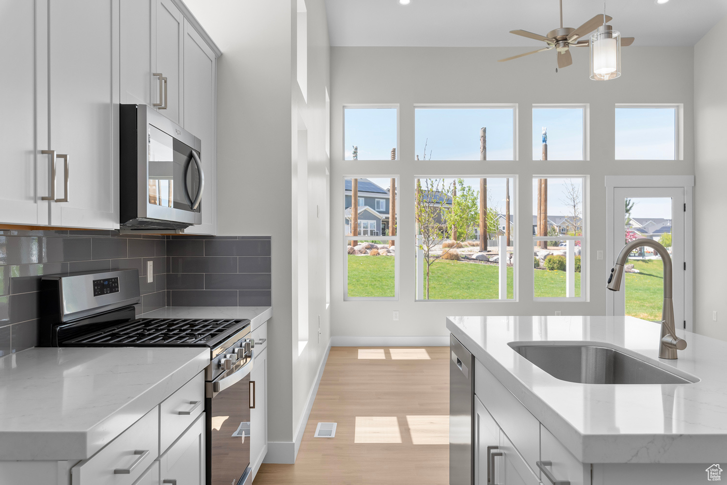 Kitchen with light hardwood / wood-style flooring, backsplash, appliances with stainless steel finishes, a center island with sink, and sink