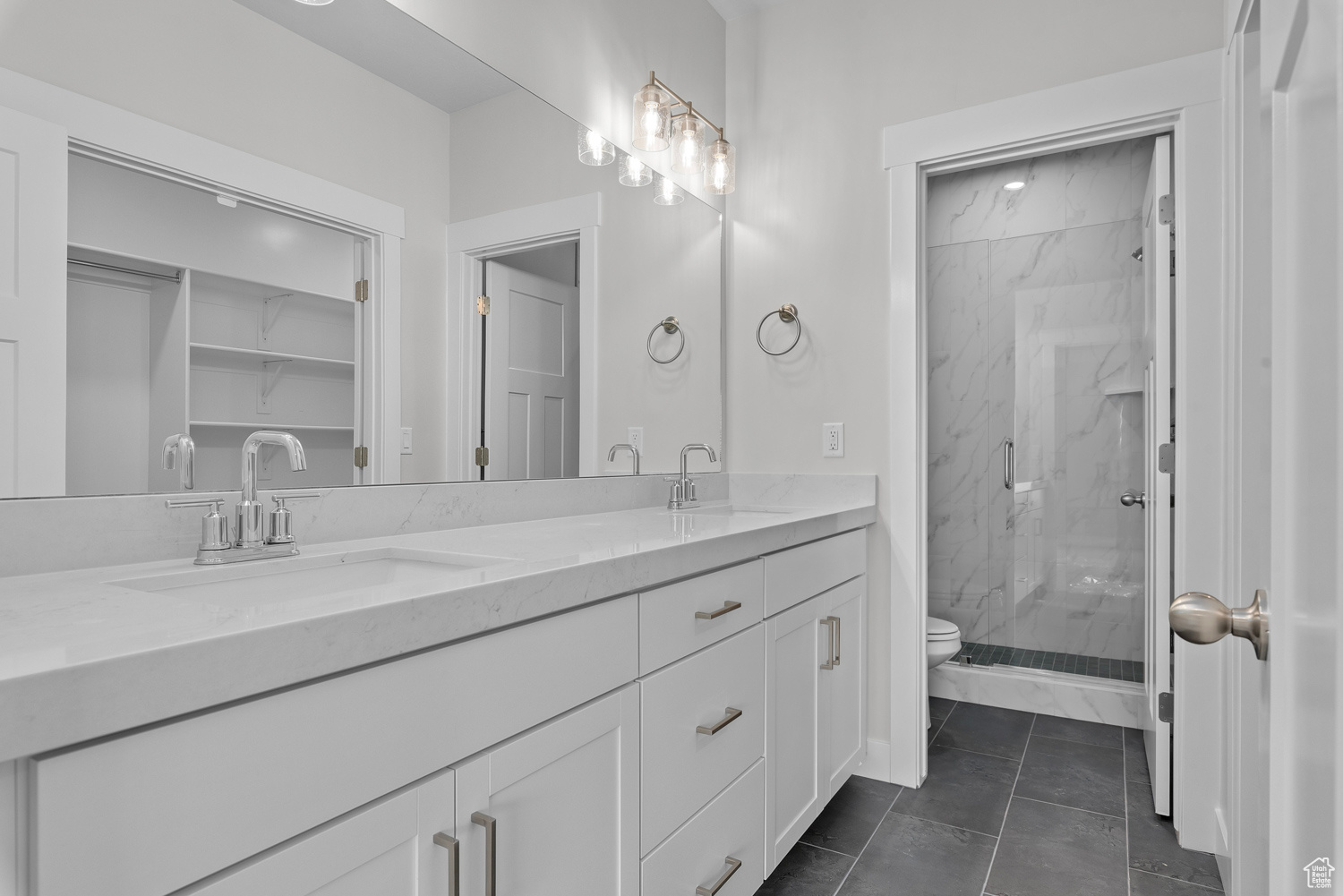 Bathroom with vanity with extensive cabinet space, an enclosed shower, tile floors, dual sinks, and toilet