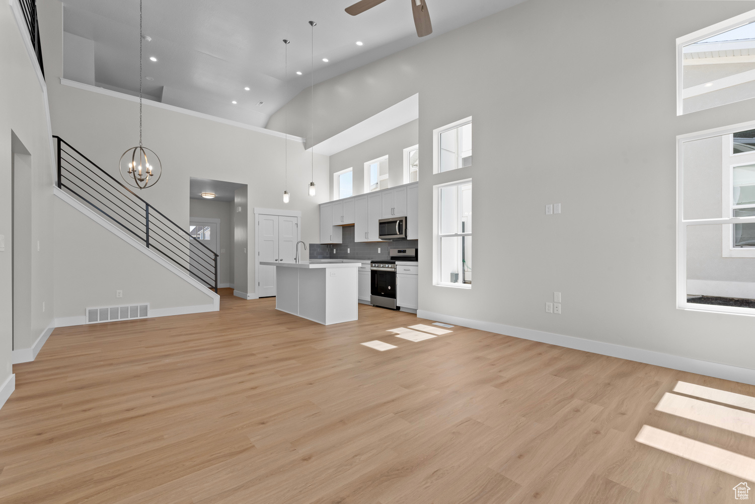 Unfurnished living room with a wealth of natural light, light hardwood / wood-style flooring, ceiling fan with notable chandelier, and high vaulted ceiling