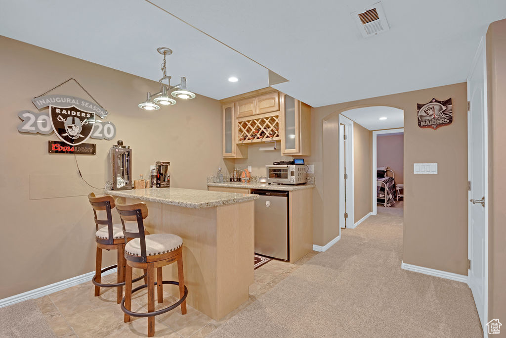 Basement Kitchen featuring pendant lighting, a breakfast bar, light tile flooring, light stone countertops, and dishwasher