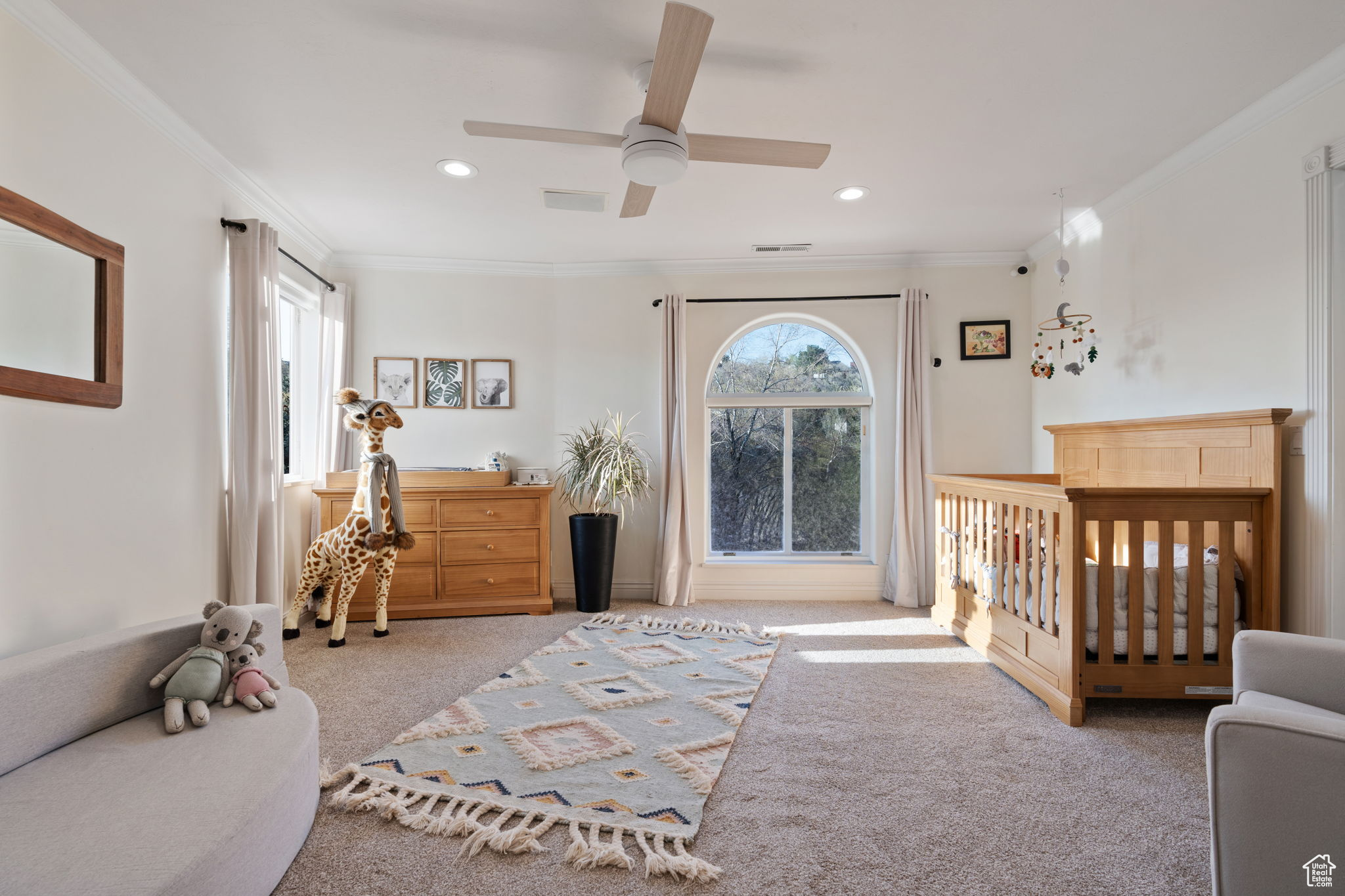 Carpeted bedroom with ceiling fan, crown molding, and a nursery area