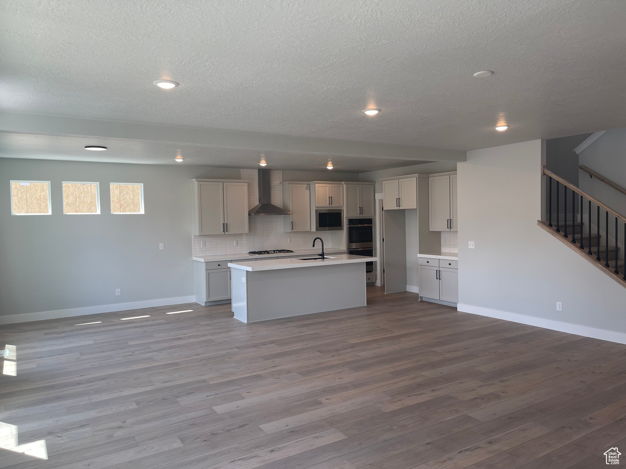 Kitchen with sink, an island with sink, hardwood / wood-style flooring, and wall chimney exhaust hood