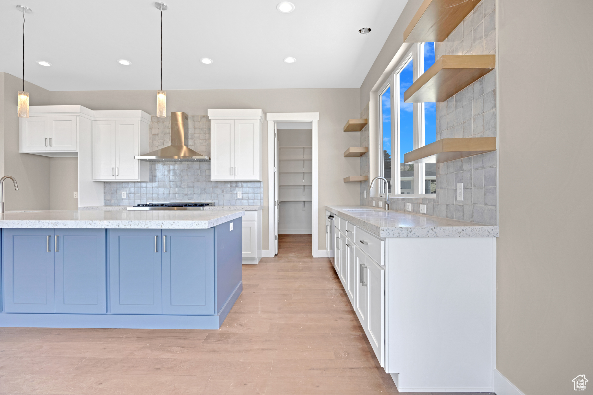 Kitchen with light hardwood / wood-style flooring, tasteful backsplash, wall chimney exhaust hood, and white cabinetry