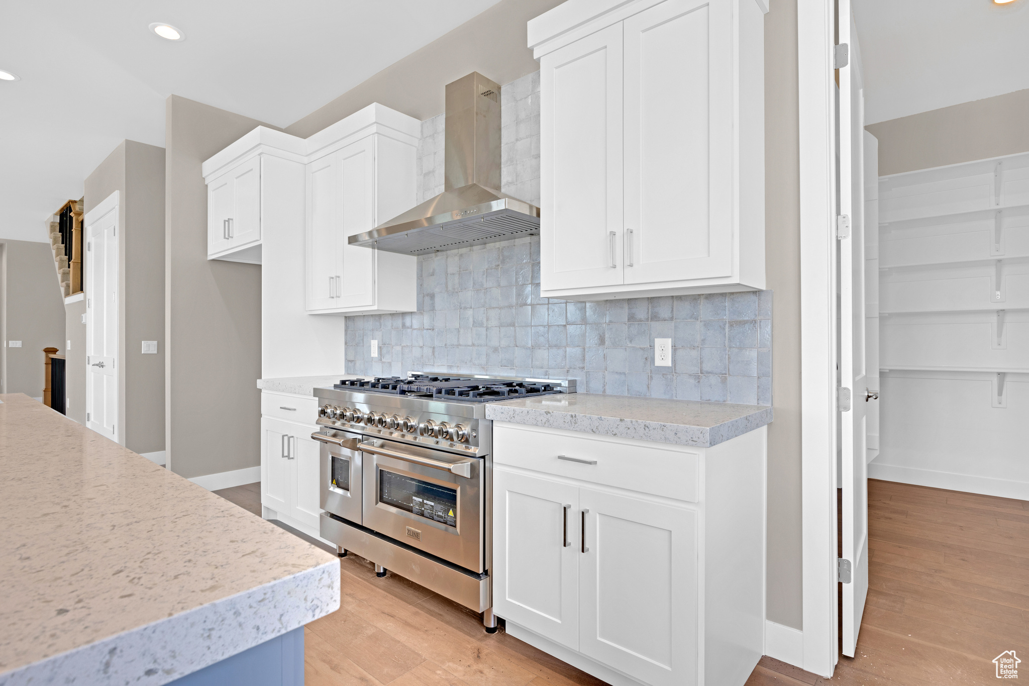 Kitchen with backsplash, double oven range, light hardwood / wood-style floors, wall chimney range hood, and white cabinets