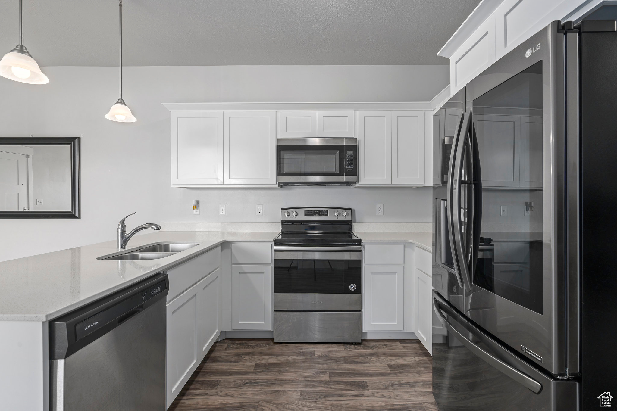 Kitchen with decorative light fixtures, appliances with stainless steel finishes,  wood-type flooring, white cabinets, and sink