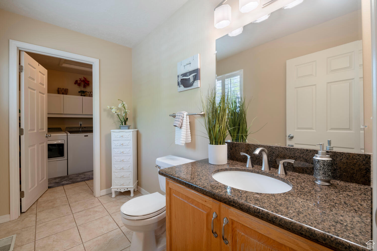 Half bathroom with tile floors and granite vanity, adjacent to washer and dryer.