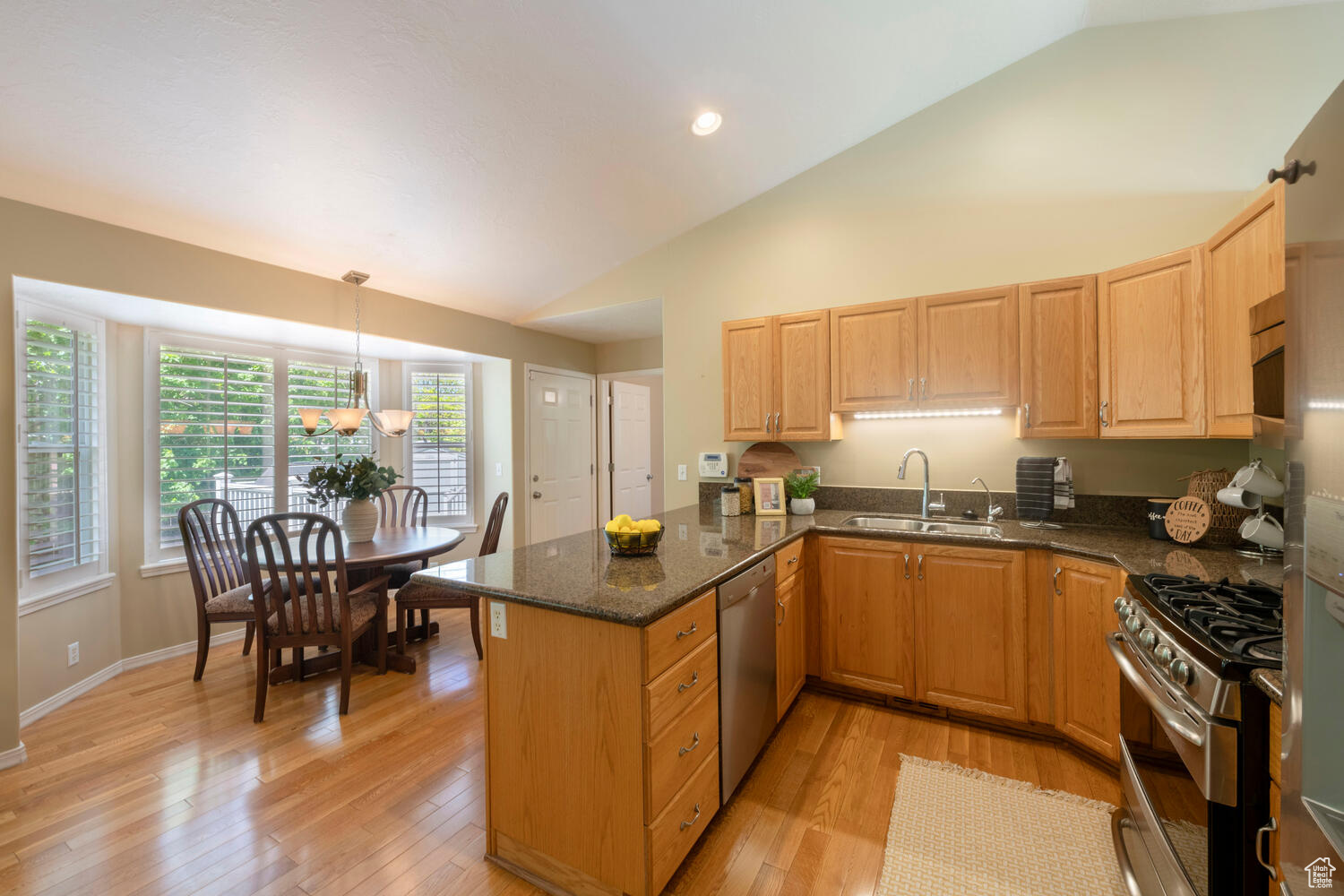 Kitchen - Dining featuring large windows, vaulted ceiling, kitchen peninsula, and light hardwood floors