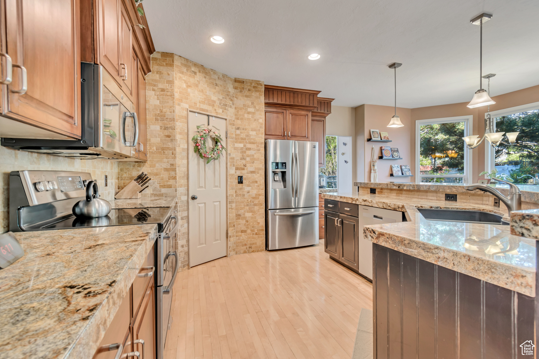 Kitchen with backsplash, stainless steel appliances, light hardwood / wood-style floors, sink, and pendant lighting