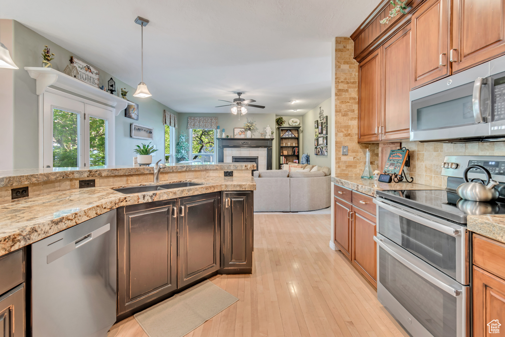 Kitchen with appliances with stainless steel finishes, ceiling fan, tasteful backsplash, light wood-type flooring, and decorative light fixtures