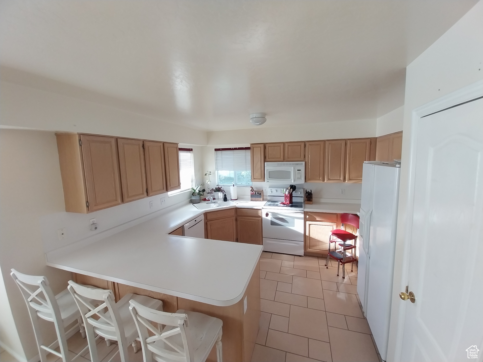 Kitchen with a kitchen breakfast bar, kitchen peninsula, white appliances, and light tile floors