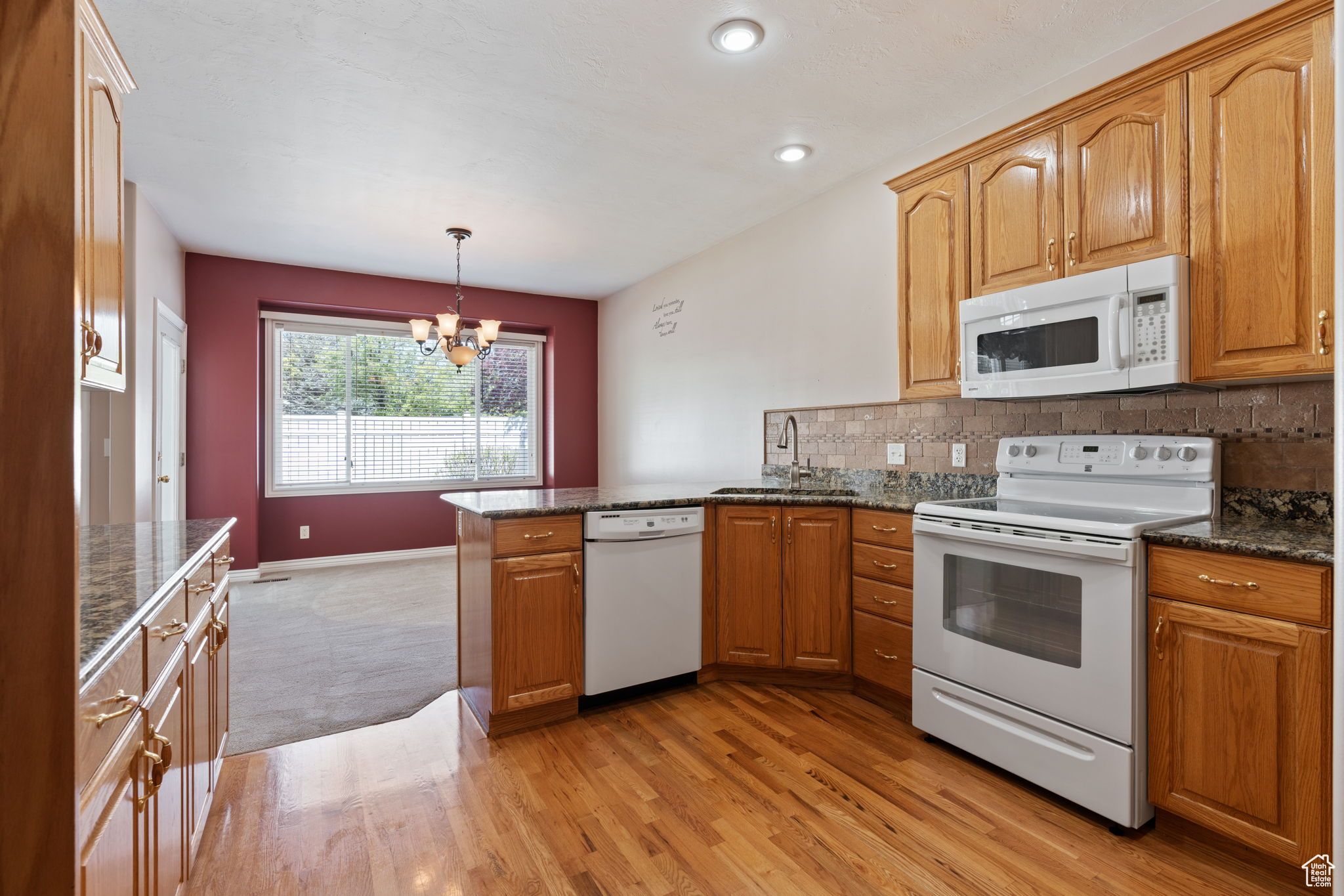 Kitchen featuring white appliances, light hardwood / wood-style floors, granite counters, sink, and a notable chandelier