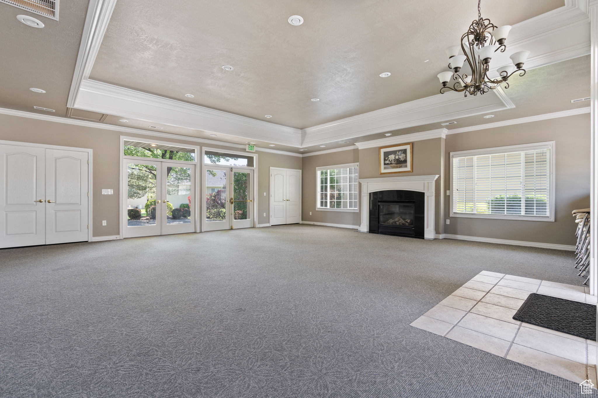 Clubhouse meeting  room featuring a raised ceiling, carpet flooring, crown molding, french doors, and an inviting chandelier
