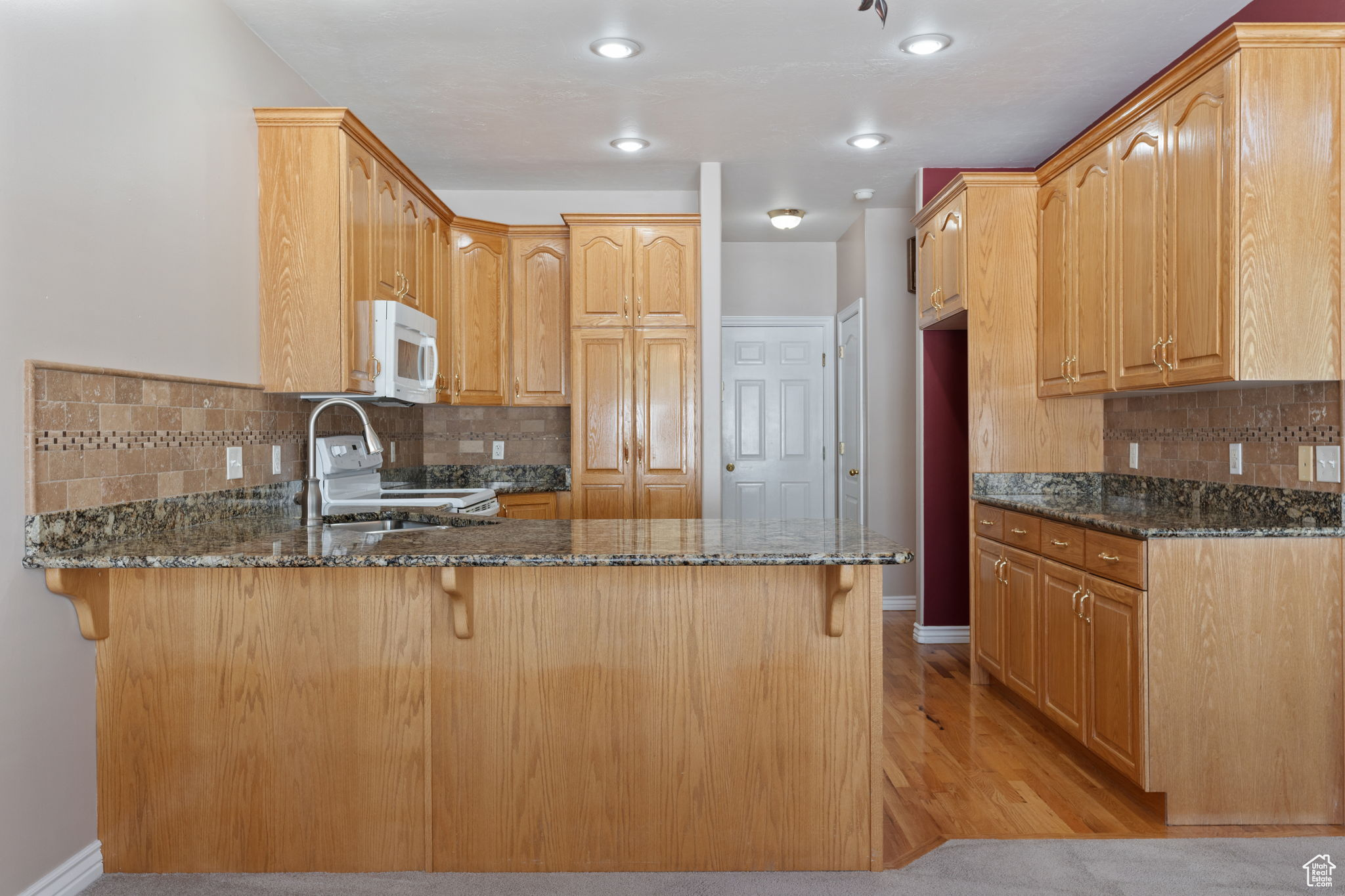 Kitchen featuring white appliances, backsplash, light wood-type flooring, and granite counters