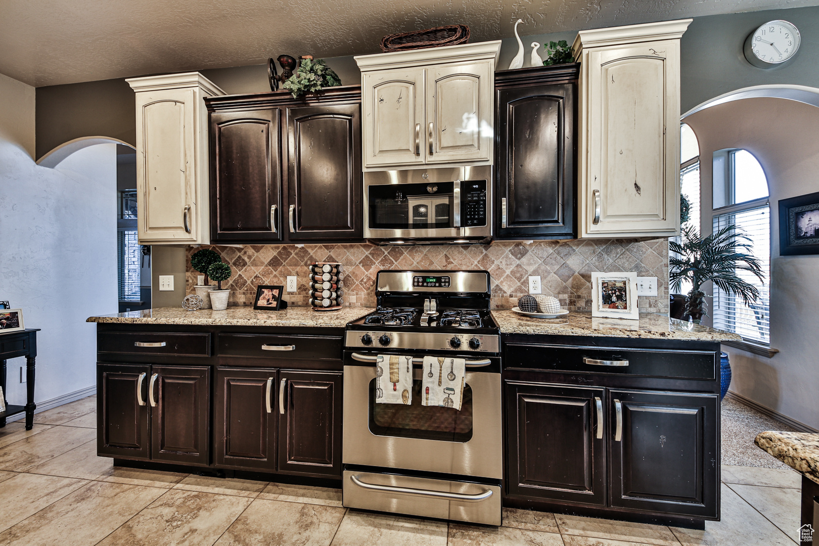Kitchen with backsplash, appliances with stainless steel finishes, light stone countertops, and light tile flooring