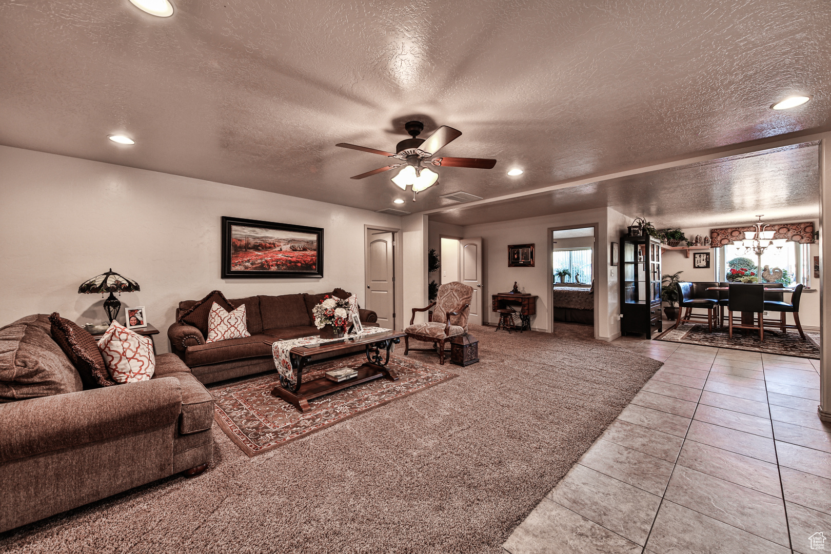 Carpeted living room with ceiling fan with notable chandelier and a textured ceiling