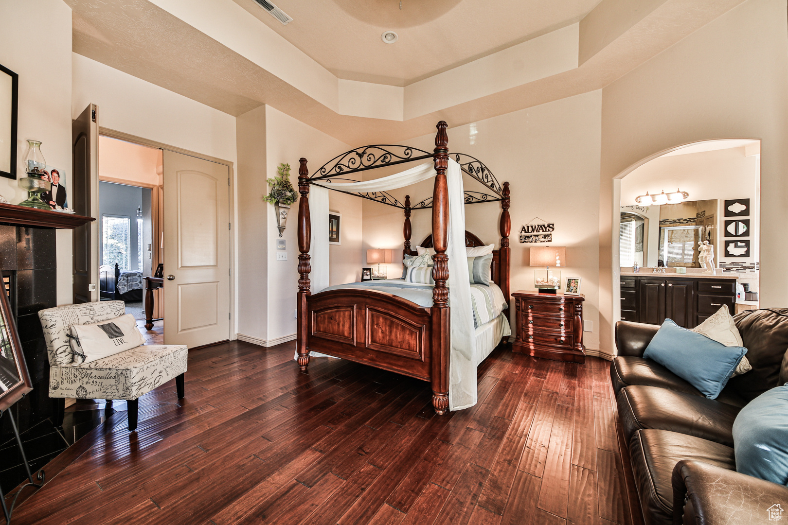 Bedroom featuring ensuite bath, dark hardwood / wood-style flooring, a tray ceiling, and a tiled fireplace