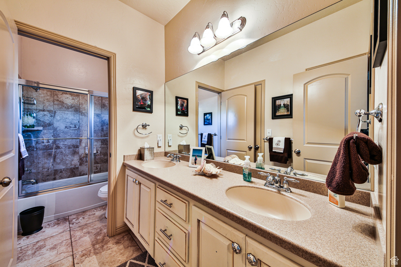 Full bathroom featuring toilet, tile flooring, dual vanity, and shower / bath combination with glass door