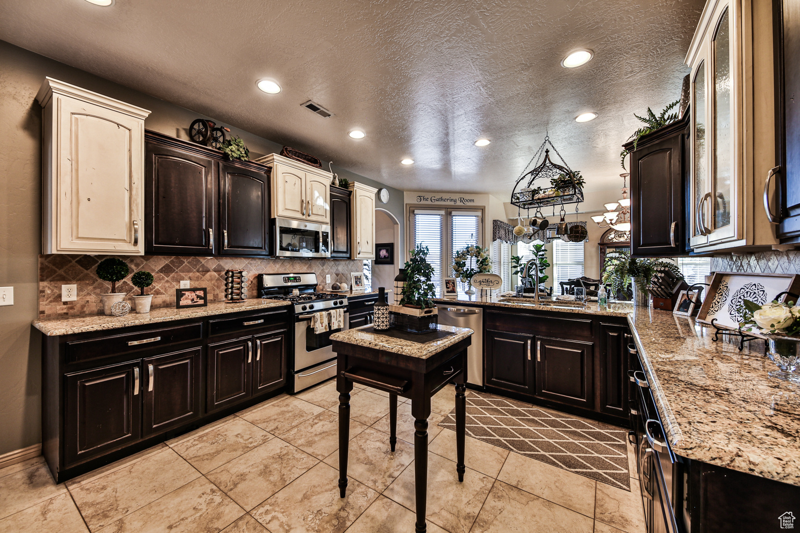 Kitchen featuring light tile flooring, stainless steel appliances, sink, tasteful backsplash, and a textured ceiling
